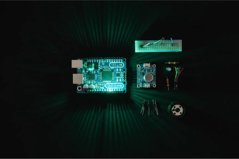 Flat-lay of Arduino and electret microphone components on black matte surface with neon green light